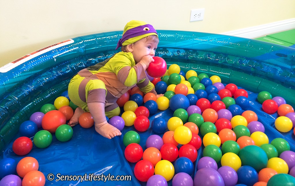 Toddler boy playing with a toy while sitting in a ball pit full of